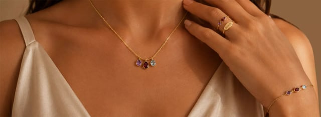 A gold necklace, ring and bracelet set with coloured stones, worn.