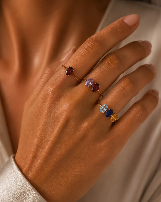 Four oval birthstone rings in different colours worn stacked across one hand